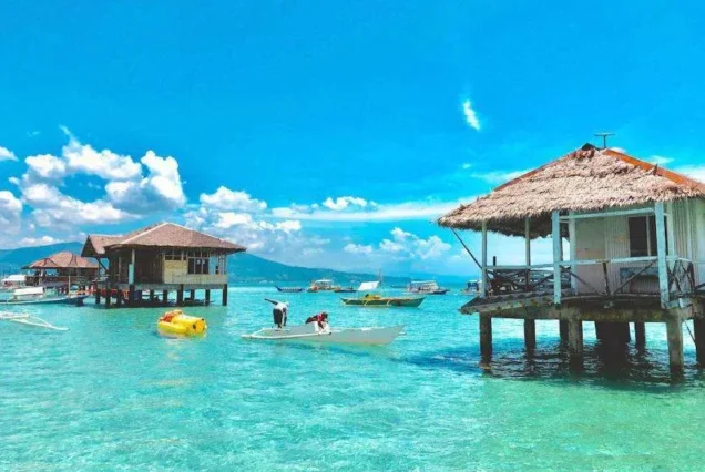 Overwater huts and boats in crystal-clear tropical sea under blue sky - highlight of Bais Dolphine Watching & Majuyod Sandbar.