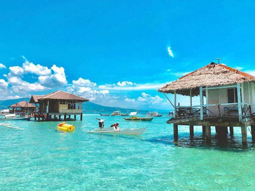 Overwater huts and boats in crystal-clear tropical sea under blue sky - highlight of Bais Dolphine Watching & Majuyod Sandbar.