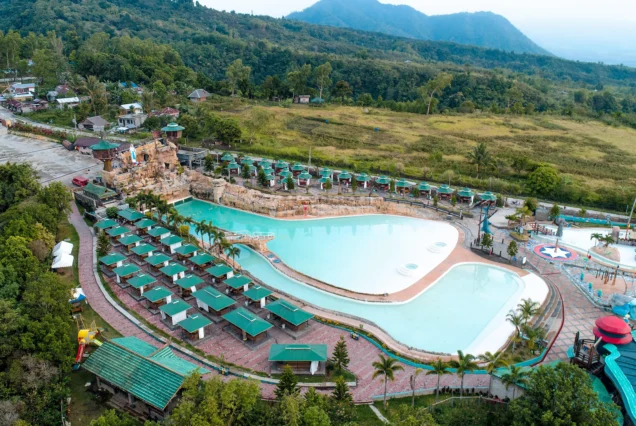 Aerial view of Campuestohan Highland Resort featuring large swimming pools, green-roofed cottages, water slides, and lush mountain scenery.