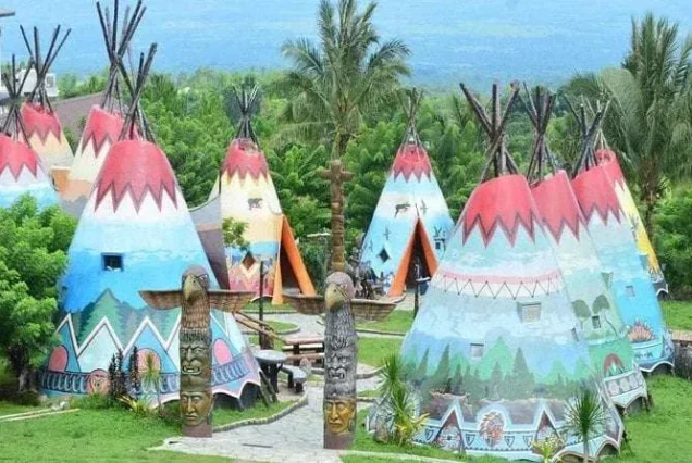 Colorful teepee-style cottages at Campuestohan Highland Resort surrounded by palm trees and mountain greenery.